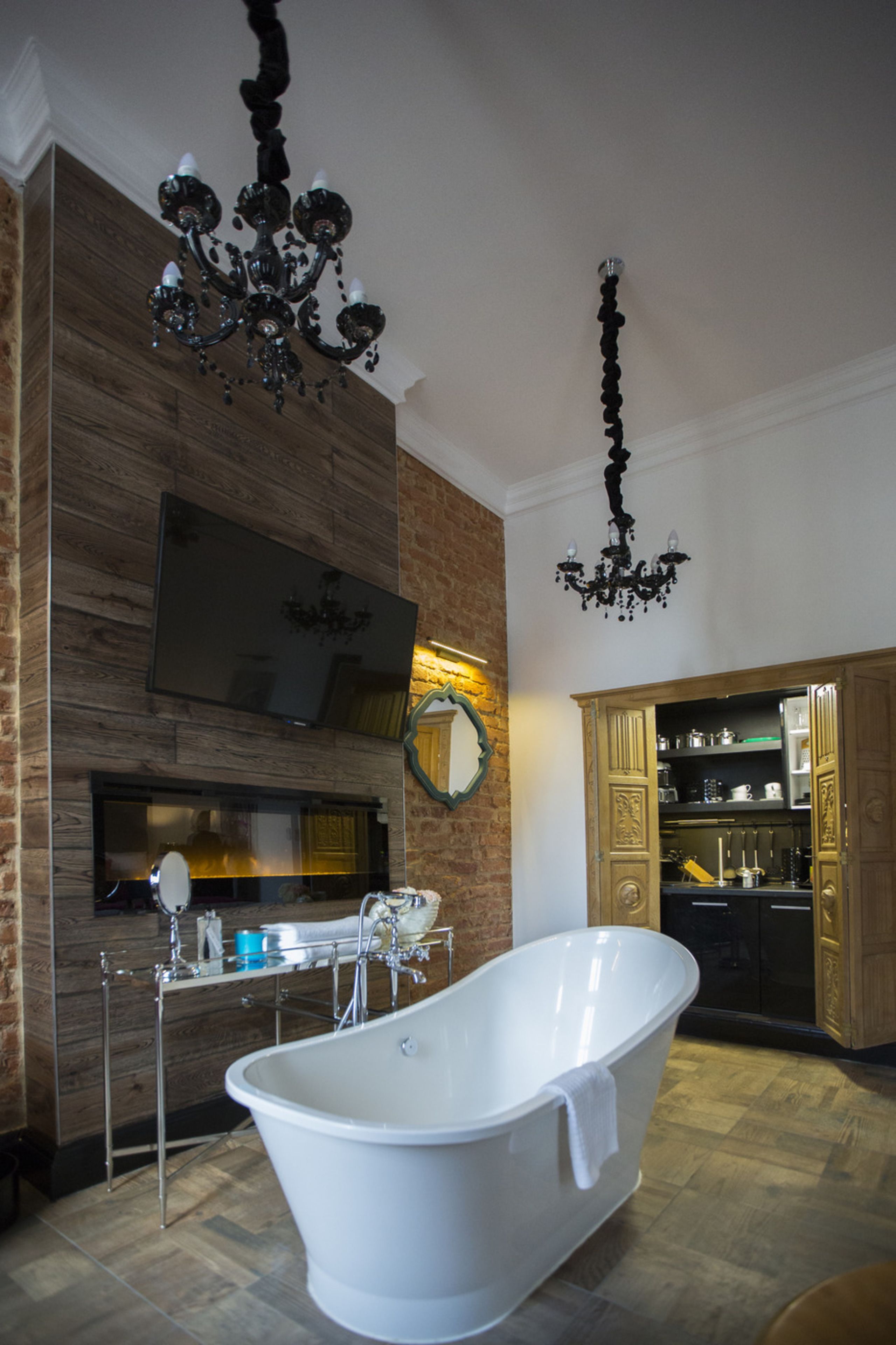A bathroom with a freestanding bathtub, a wooden wall, a mirror, and a chandelier.
