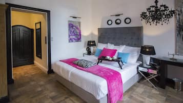 Un dormitorio con cama, mesitas de noche, una araña y una puerta que da a otra habitación.