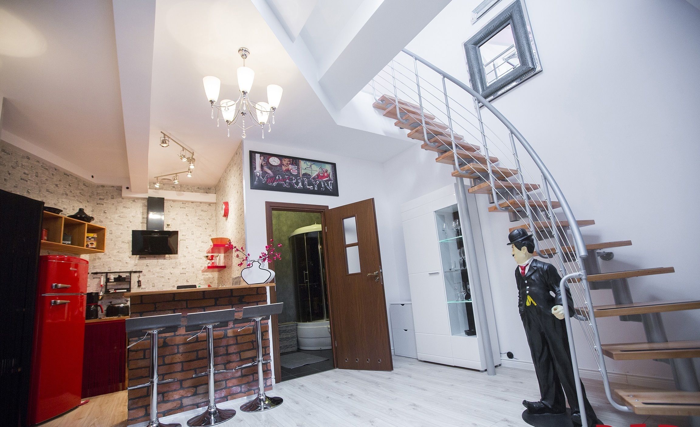 A modern kitchen with a red refrigerator, a wooden bar counter, and a chandelier.