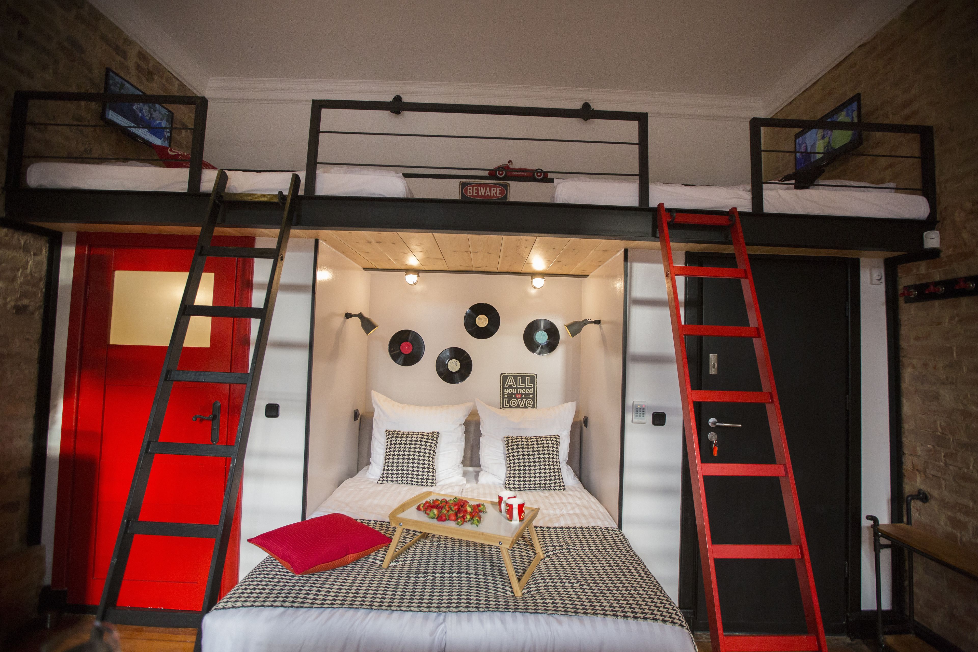 Habitación con literas, una puerta roja, dos escaleras, una bandeja con fruta y adornos en la pared.