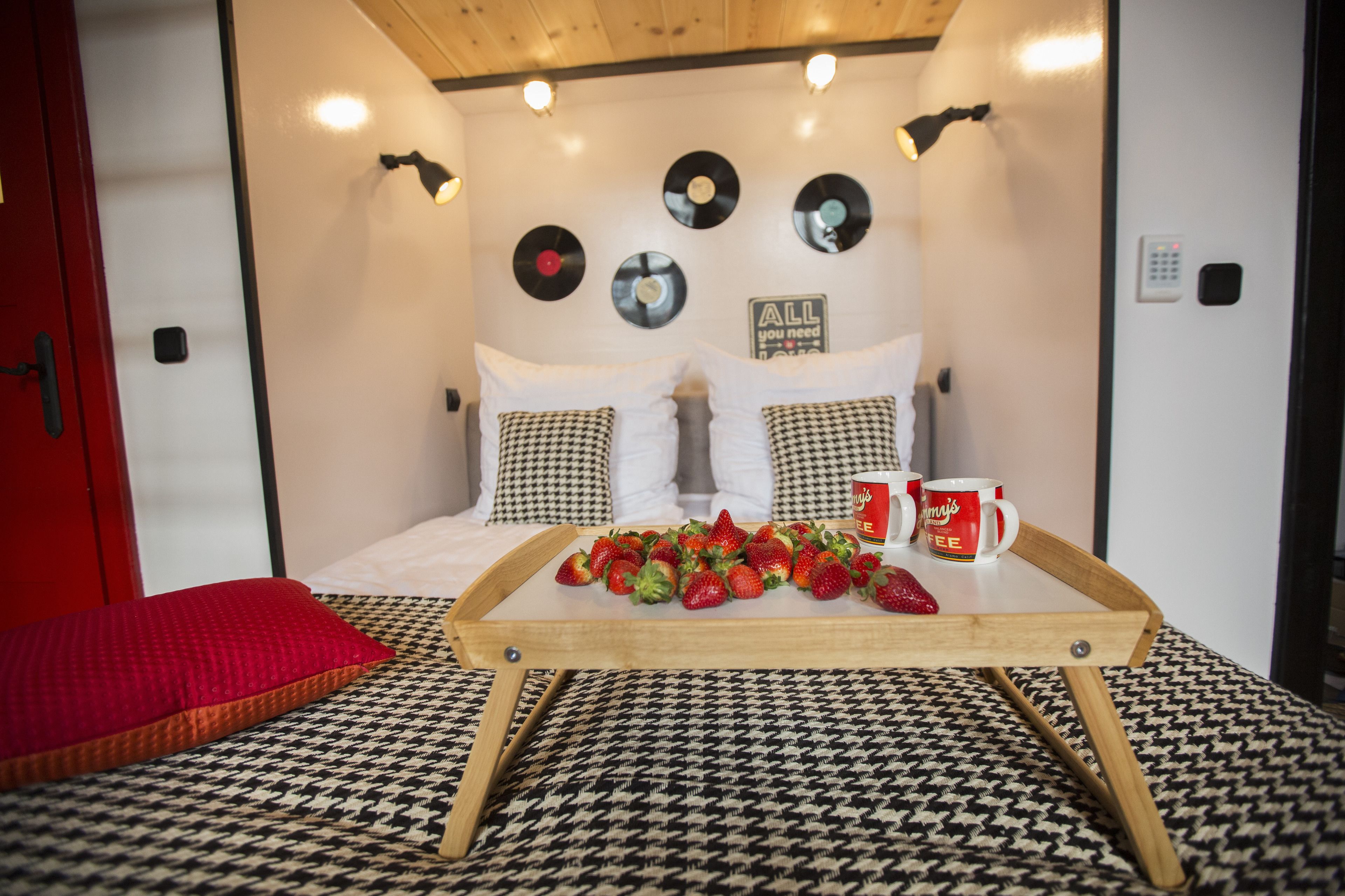 Un dormitorio acogedor con cama, almohadas a cuadros, una bandeja de fresas y una pared con discos de vinilo.