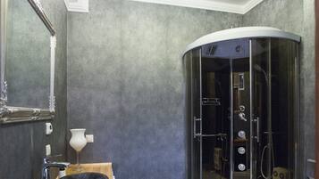 A modern bathroom with a curved glass shower enclosure, a white sink, and a large mirror.