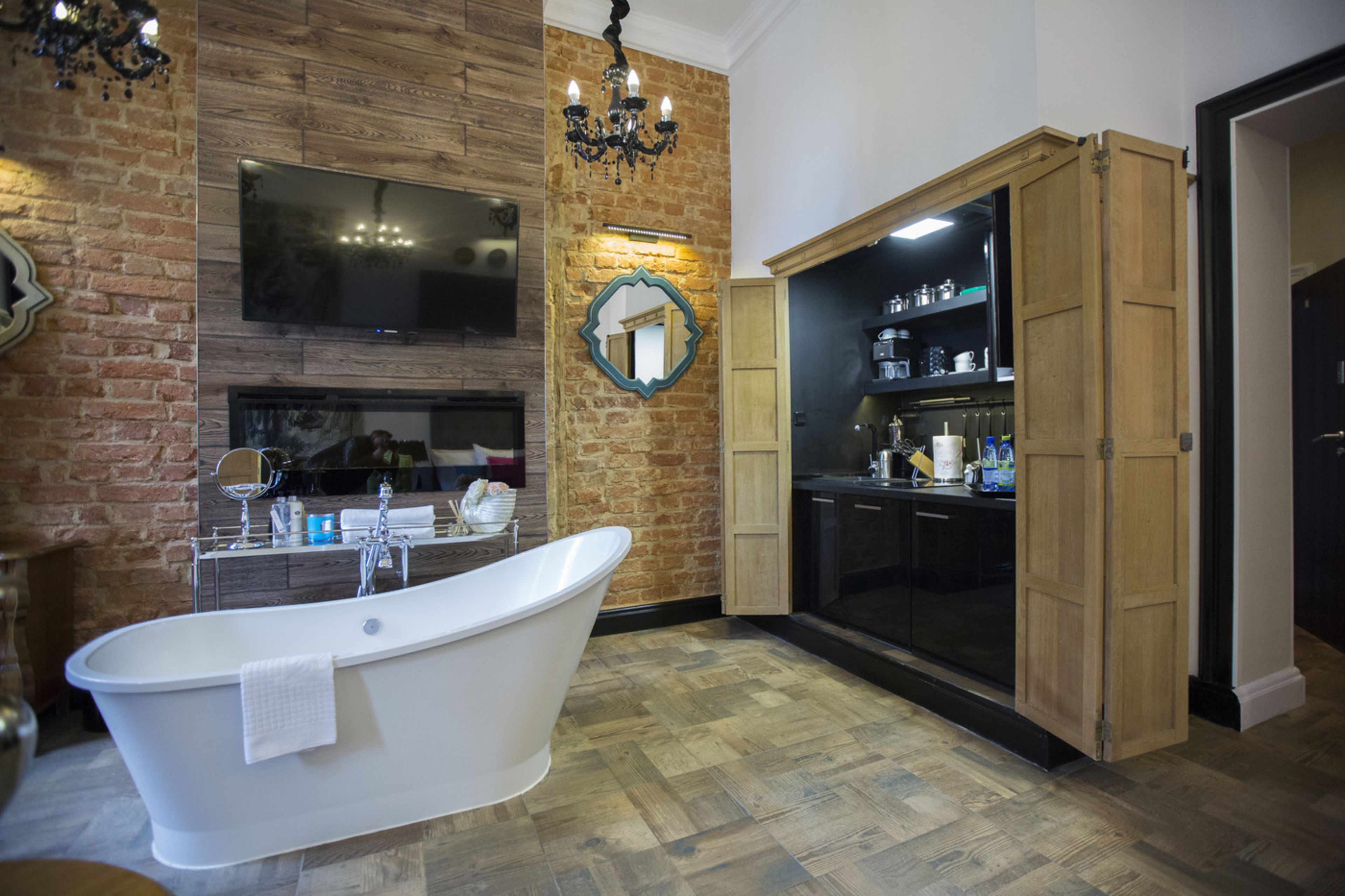A bathroom with a freestanding bathtub, a large mirror, a chandelier, and a wooden cabinet.
