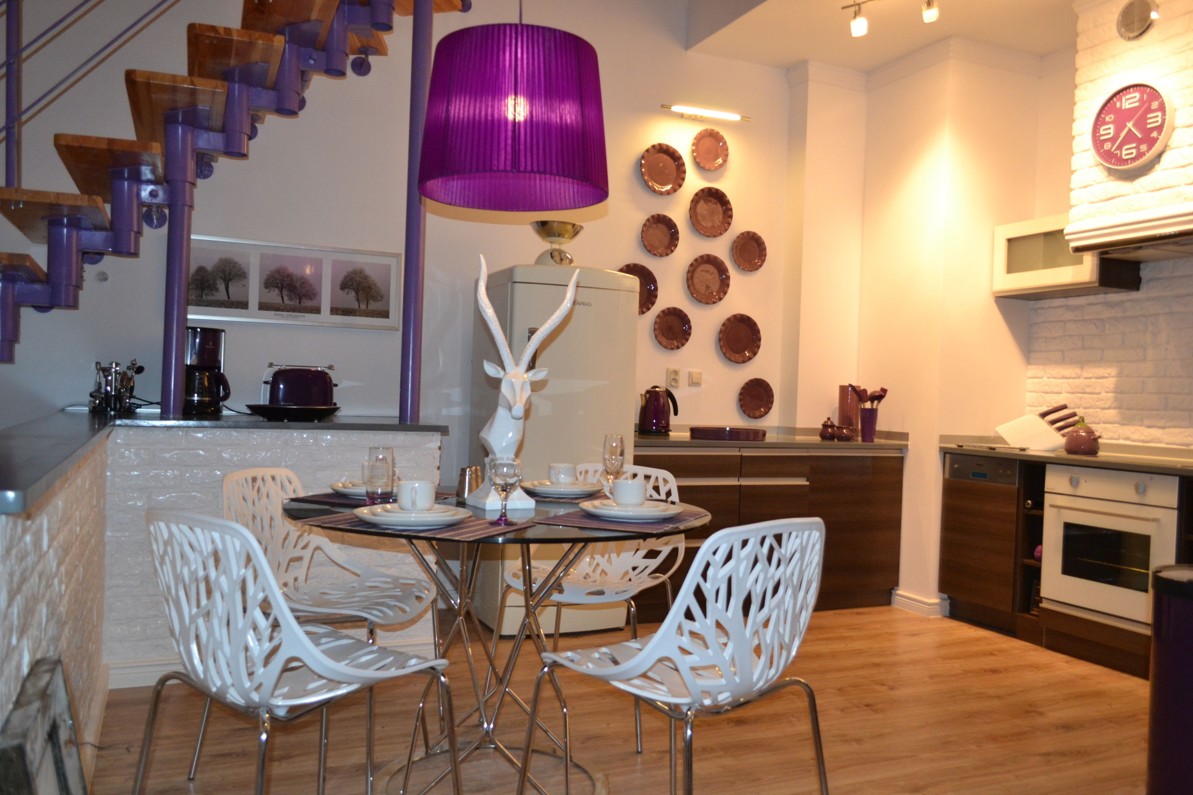 Eine moderne Küche mit Essbereich, inklusive Treppe, einer violetten Pendelleuchte und einer Wand mit dekorativen Tellern.