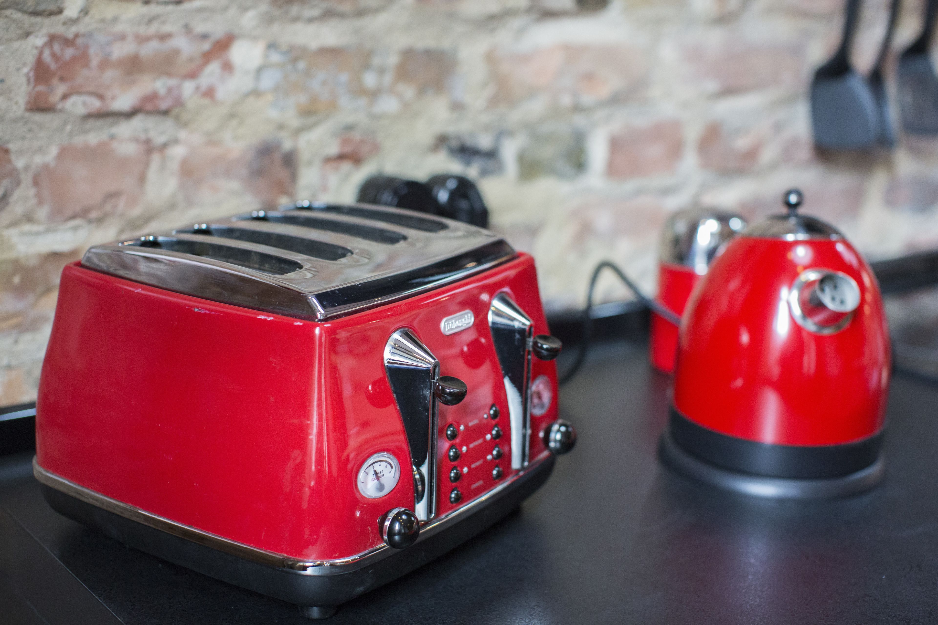 Een rode toaster en een rode waterkoker op een zwart aanrecht tegen een bakstenen muur.
