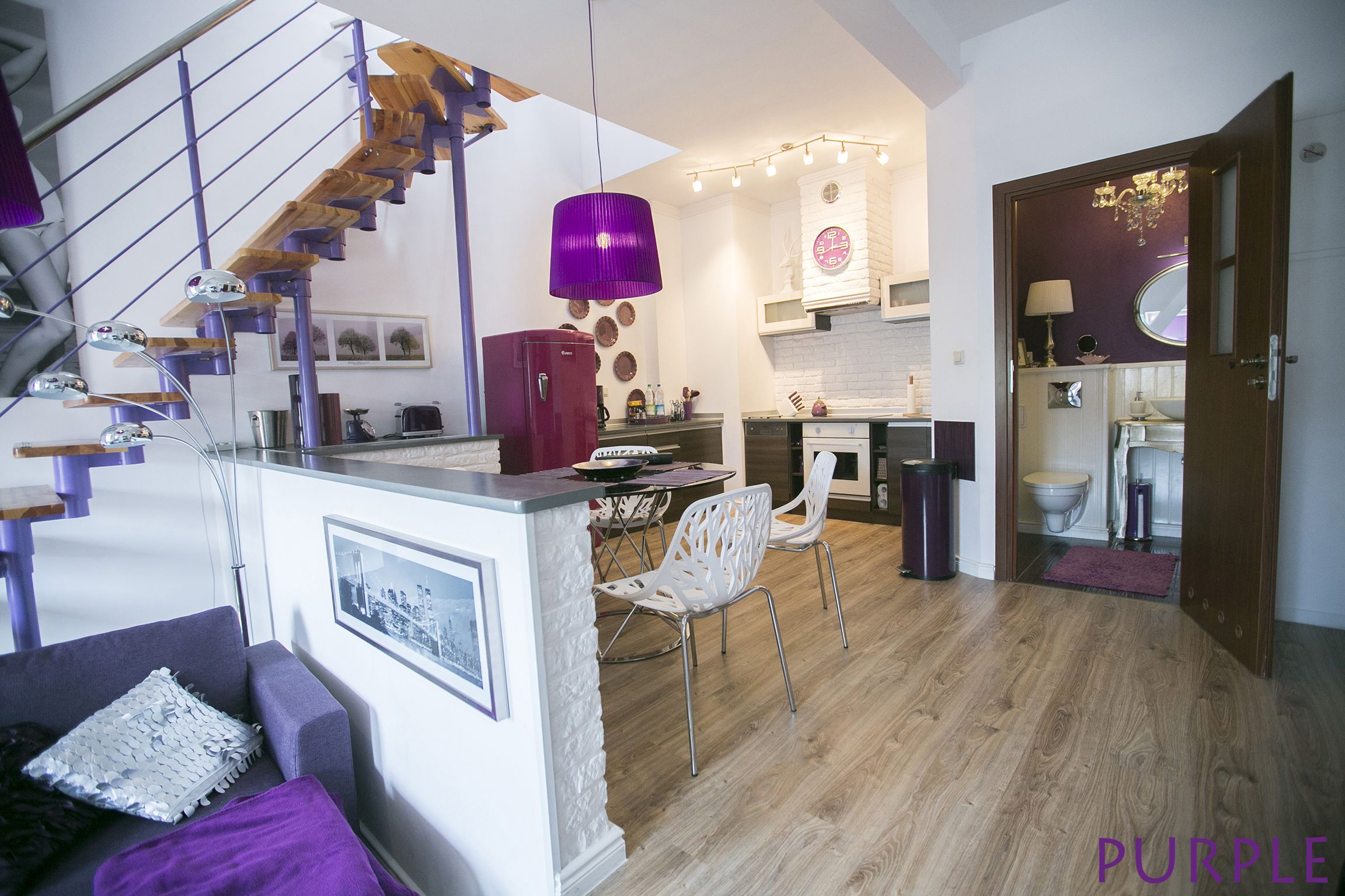Eine moderne Küche mit einer Holztreppe, weißen Wänden und einer violetten Pendelleuchte.