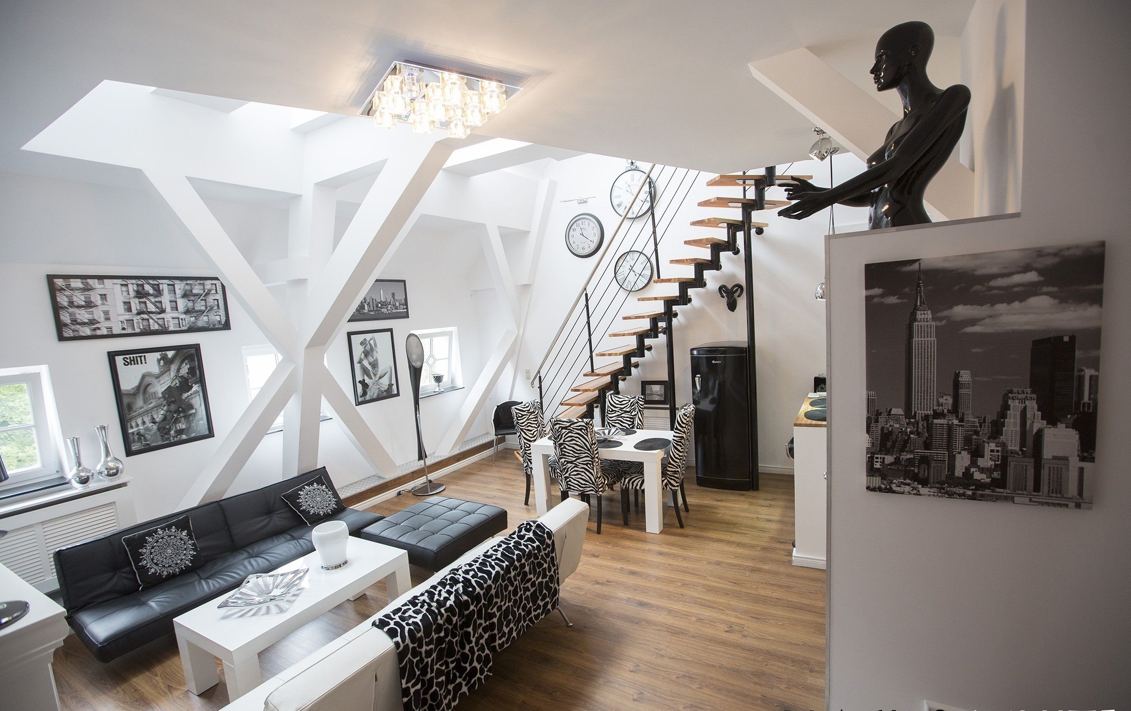 A modern living room with a black and white sofa, a zebra-patterned ottoman, a white coffee table, and a staircase with a black railing.
