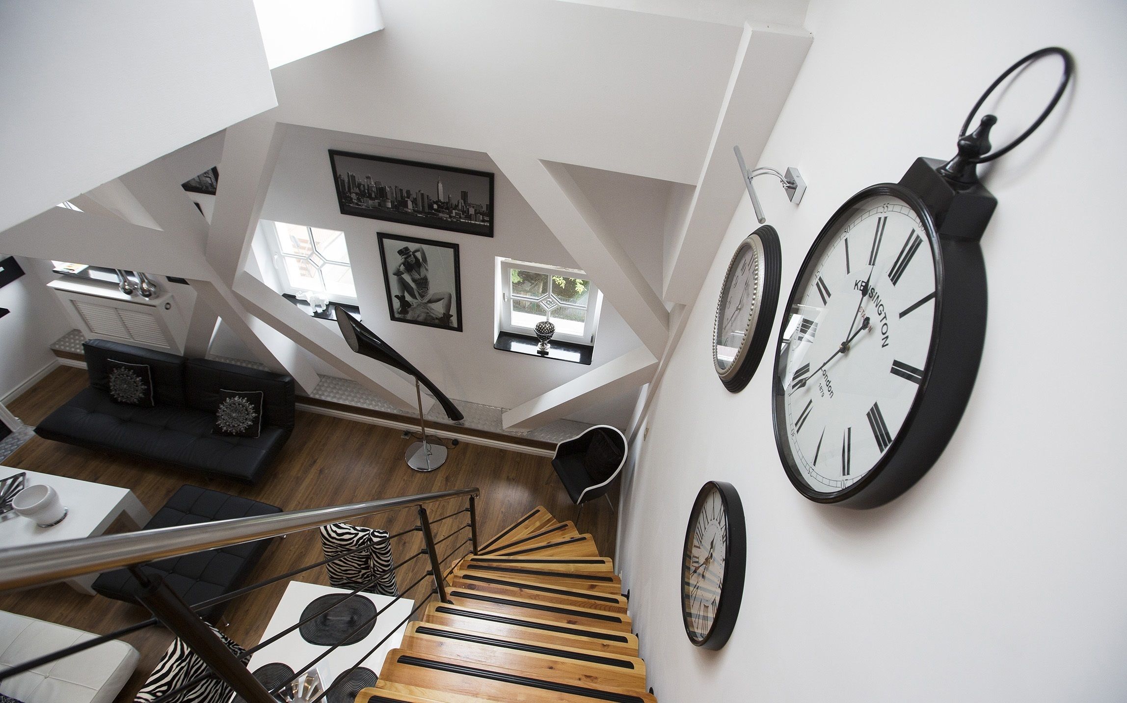 Un interior moderno con una escalera, un sofá de cuero negro y varios relojes de pared.
