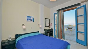 A bedroom with a bed, bedside table, lamp, and a view of the sea through an open door. - Dilino Hotel (Naxos)