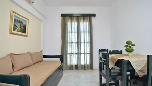 A room with a sofa, a dining table with chairs, a potted plant, and a window with curtains. - Dilino Hotel (Naxos)