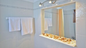 A bathroom with white tiled walls, a large mirror, and a shelf with towels. - Dilino Hotel (Naxos)