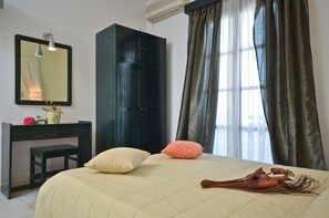 A bedroom with a bed, a dark wardrobe, a desk with a chair, a mirror, and a window with curtains. - Dilino Hotel (Naxos)