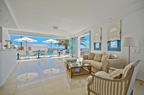 A spacious living room with a large window, a sofa, a coffee table, and a view of the pool and ocean. - Dilino Hotel (Naxos)