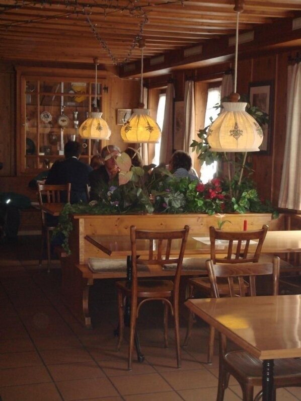 Un restaurante acogedor con interiores de madera, lámparas colgantes y una mesa central rodeada de sillas.