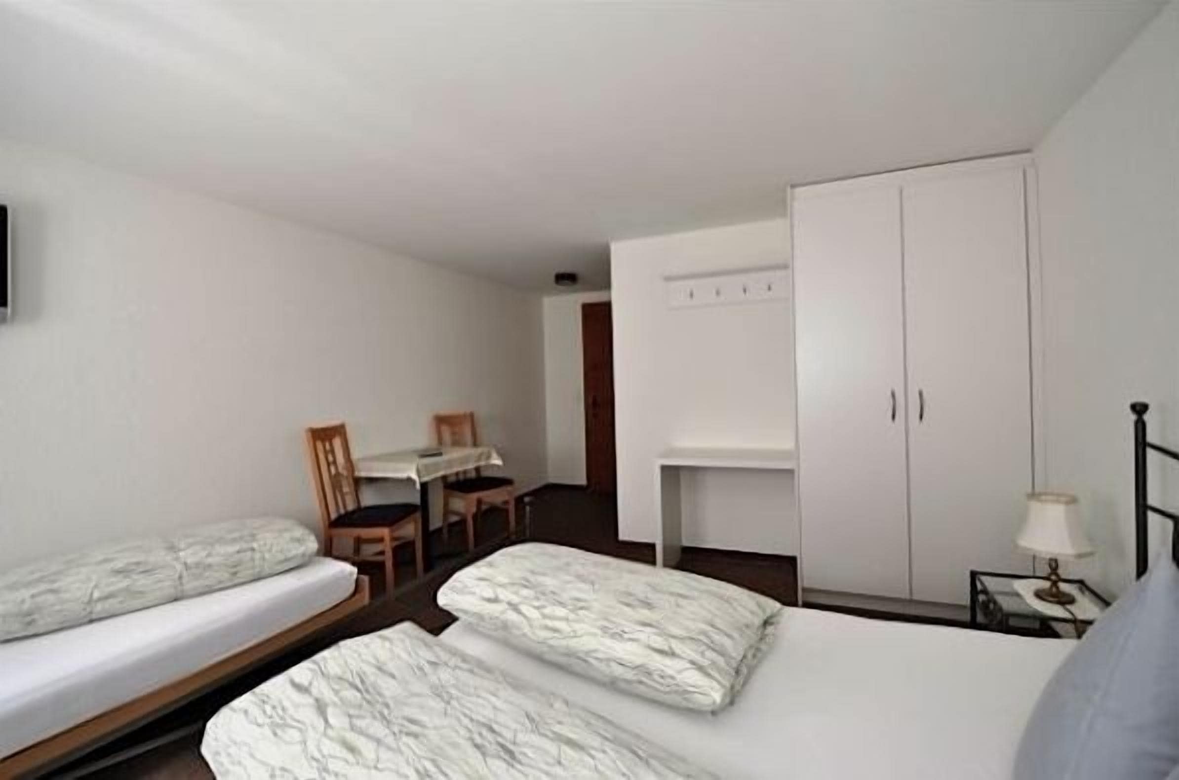 Ein kleines, schlichtes Zimmer mit zwei Einzelbetten, einem Schreibtisch und einem Stuhl.