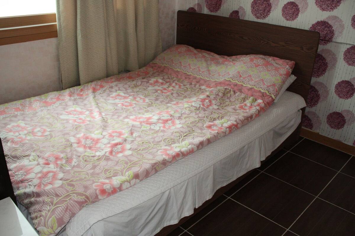 A single bed with a floral bedspread, a wooden headboard, and a wall with a circular pattern.