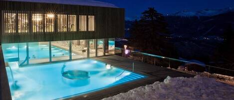 Un edificio moderno con zona de piscina cubierta de cristal y terraza de madera.