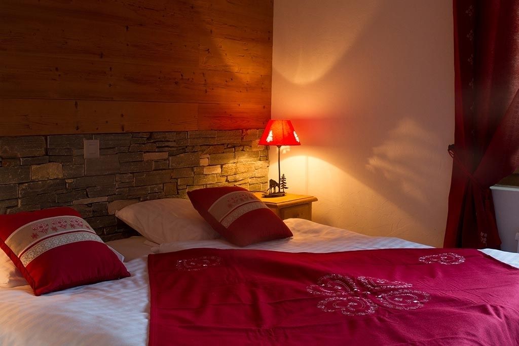 Een slaapkamer met een stenen muur, een houten hoofdbord, een rode lamp en een bed met rode beddengoed.