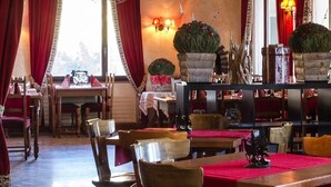 A cozy restaurant interior with wooden furniture, red curtains, and decorative plants. - Hotel-Restaurant de la Poste (Ayent)