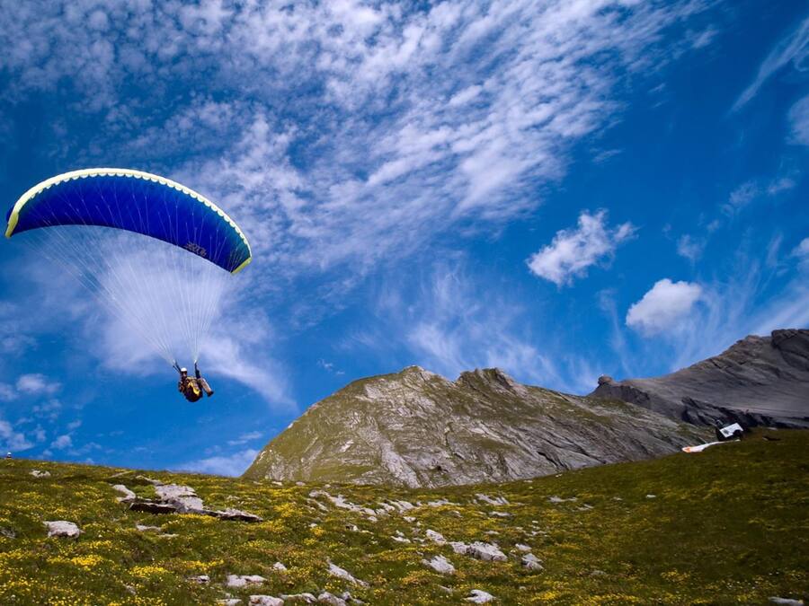Uma pessoa praticando parapente sobre uma paisagem montanhosa sob um céu claro.