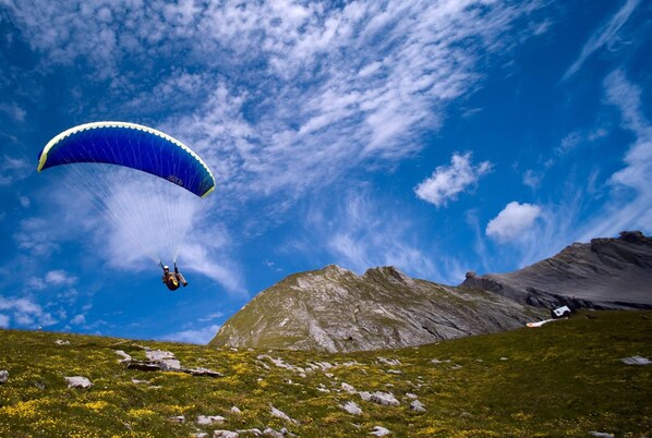 A person paragliding over a mountainous landscape with a clear sky. - Hotel-Restaurant de la Poste (Ayent)