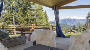 An outdoor seating area with a view of snow-capped mountains, wooden furniture, and a rustic wooden fence. - Hotel-Restaurant de la Poste (Ayent)