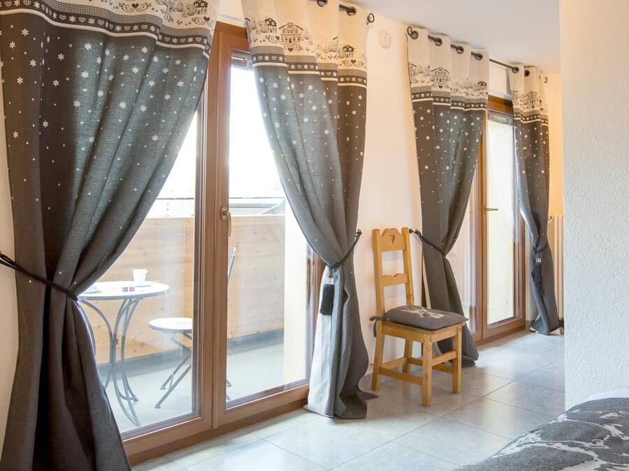 Una habitación con una silla de madera, una mesita y un sofá. Las cortinas presentan un diseño con casas y estrellas.