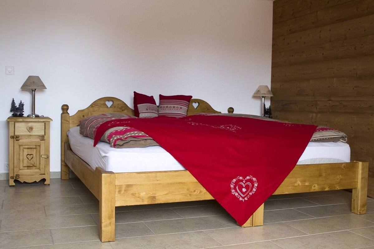 A wooden bed with a red blanket, two bedside tables with lamps, and a small cabinet with a heart design.