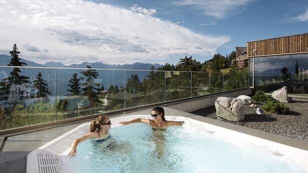 A hot tub with a clear view of mountains and a modern building in the background. - Hotel-Restaurant de la Poste (Ayent)