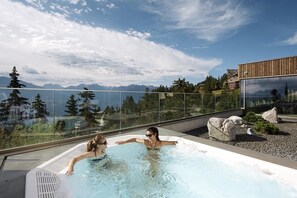 A hot tub with a clear view of mountains and a modern building in the background. - Hotel-Restaurant de la Poste (Ayent)