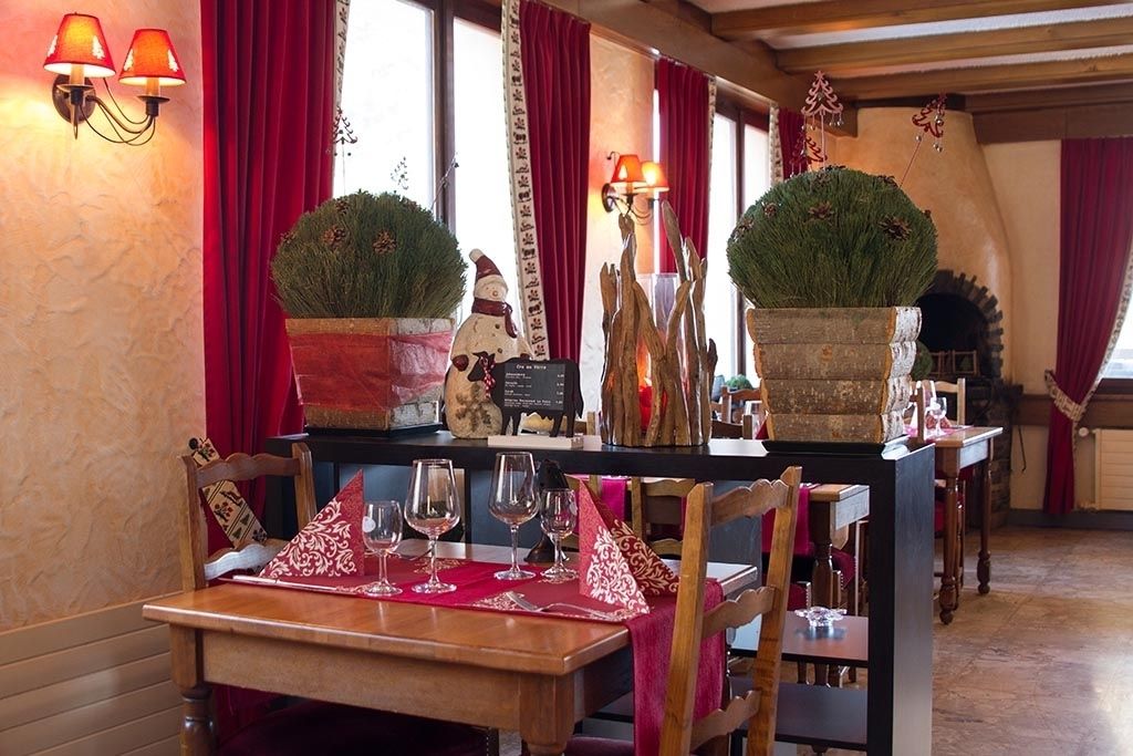Ein gemütliches Restaurant-Interieur mit Holztischen, roten Vorhängen und dekorativen Topfpflanzen.