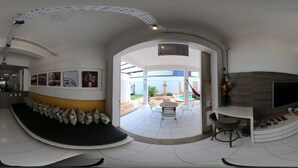 A modern living room with a curved sofa, a flat-screen TV, and a dining area with chairs and a table. - Albergaria Hostel & Bar (Fortaleza)