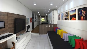 A modern hotel lobby with a reception desk, a TV, a fan, and a row of colorful pillows. - Albergaria Hostel & Bar (Fortaleza)