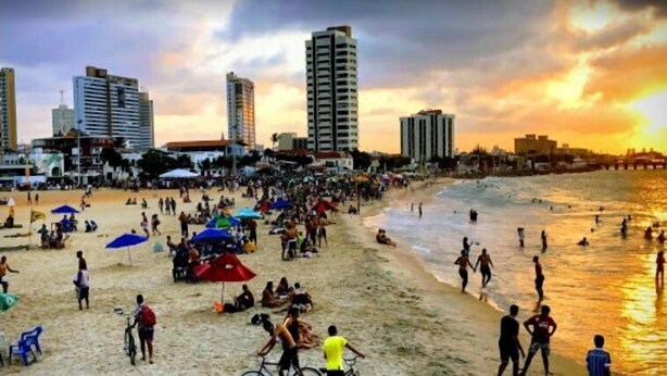 A crowded beach with people, umbrellas, and buildings in the background. - Albergaria Hostel & Bar (Fortaleza)