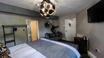Et soveværelse med seng, garderobeskab, skrivebord, fjernsyn og en loftlampe.