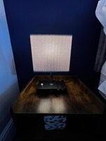Una mesita de noche con una lámpara y un objeto decorativo sobre una superficie de madera.