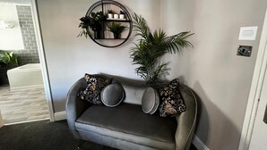 A grey sofa with patterned cushions, a wall-mounted plant shelf, and a door leading to a bathroom. - Elephant & Castle (Holmfirth)