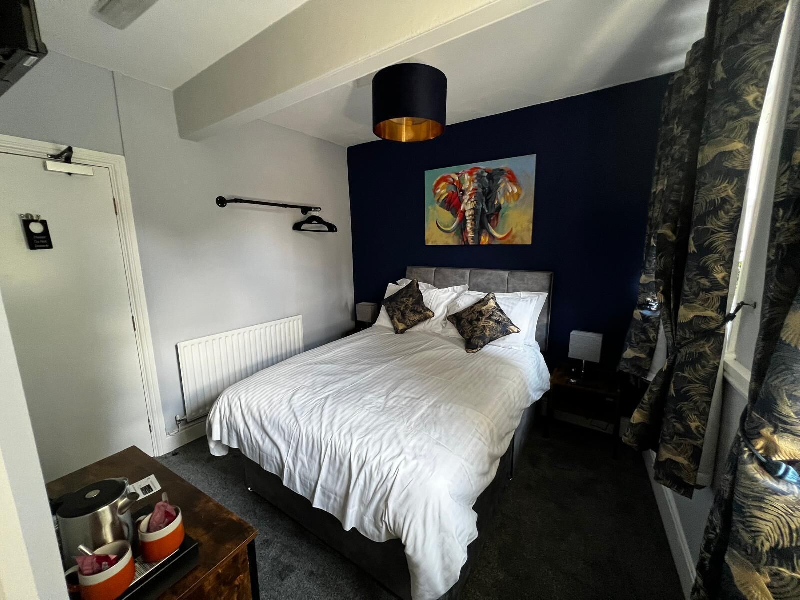 A neatly arranged bedroom with a bed, bedside tables, a radiator, and a painting on the wall.