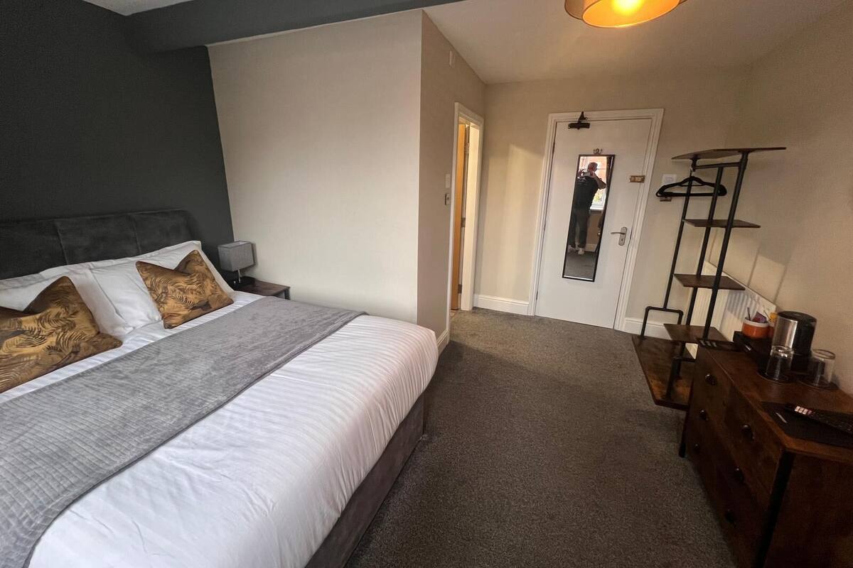A bedroom with a bed, bedside tables, a dresser, a mirror, and a hanging shelf.