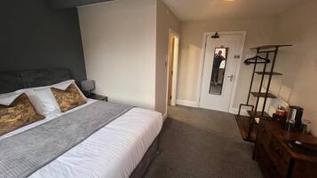 Un dormitorio con cama, mesitas de noche, cómoda, espejo y estante colgante.