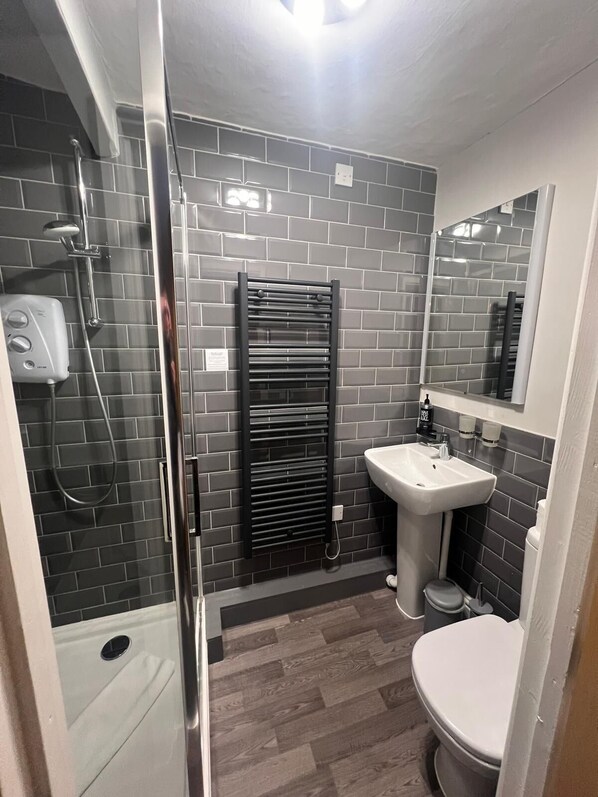 Un baño moderno con cabina de ducha de vidrio, toallero negro, lavamanos blanco y un inodoro.
