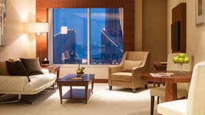 A modern living room with a sofa, armchairs, a coffee table, and a dining table. A large window offers a view of a cityscape and a bridge. - Carlton Downtown (Dubai)