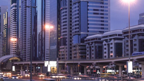 A cityscape with modern skyscrapers, a curved bridge, and a busy street with vehicles. - Carlton Downtown (Dubai)