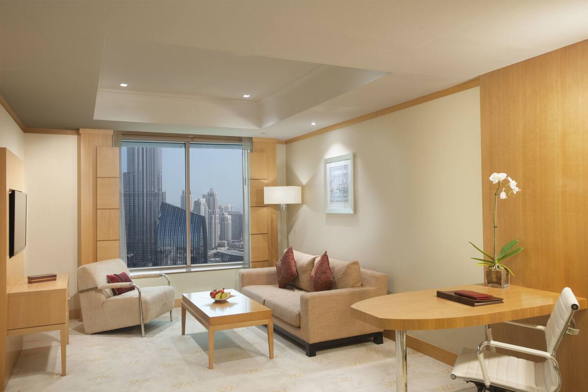 Une chambre d’hôtel moderne dotée d’une grande fenêtre donnant sur la ville, d’un canapé, d’une table à manger et d’une petite plante en pot.