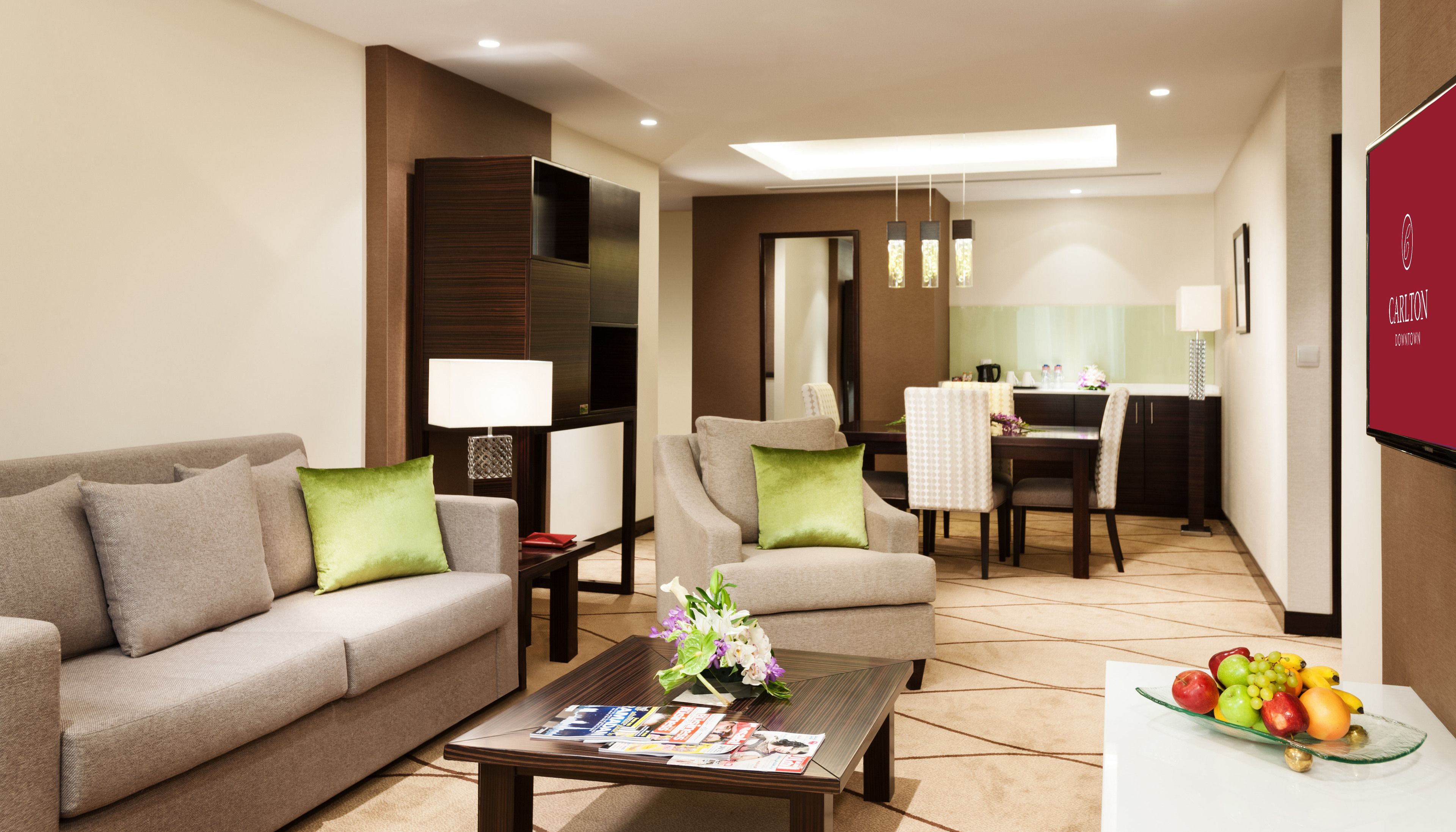 A hotel room with a sofa, armchair, dining table, and a coffee table with magazines and flowers.