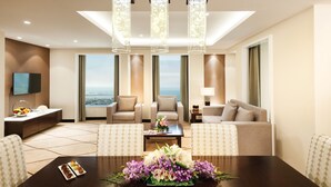 A modern hotel lobby with a large dining table, comfortable seating, a TV, and a city view. - Carlton Downtown (Dubai)