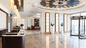 A modern hotel lobby with a reception desk, seating area, and a large chandelier. - Carlton Downtown (Dubai)