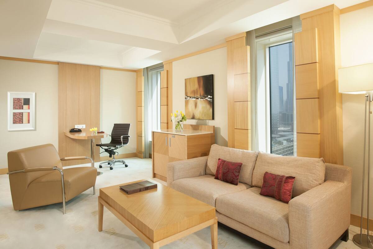Une chambre d’hôtel moderne équipée d’un canapé, d’un fauteuil, d’un bureau et d’une grande fenêtre donnant sur la ville.