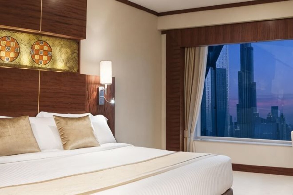 A hotel room with a large bed, a cityscape view, and a wall-mounted light fixture.