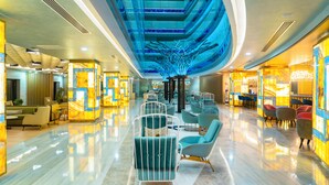 A modern hotel lobby with a central seating area, a high ceiling with a blue light feature, and a reception desk on the right. - Royal Wings Hotel - All Inclusive (Antalya)